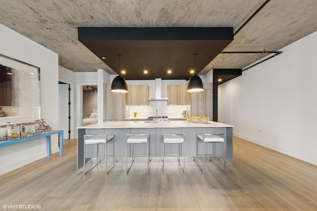 kitchen with a breakfast bar area, light wood-style flooring, wall chimney exhaust hood, and modern cabinets