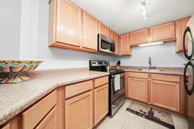 kitchen featuring light brown cabinets, appliances with stainless steel finishes, light tile patterned floors, and a sink