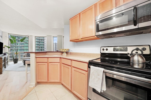 kitchen with light tile patterned floors, a peninsula, stainless steel appliances, light countertops, and light brown cabinets