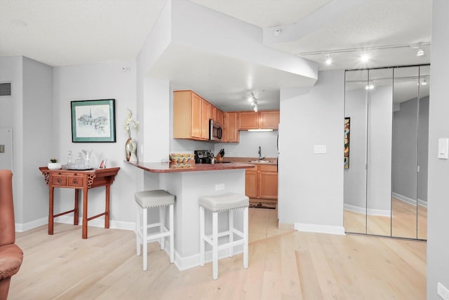 kitchen featuring a breakfast bar, stainless steel appliances, visible vents, light wood-style flooring, and a peninsula