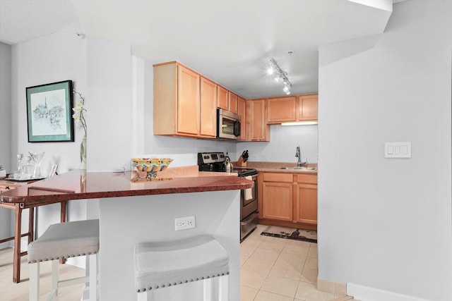 kitchen with light tile patterned floors, stainless steel appliances, light brown cabinetry, a sink, and a kitchen breakfast bar