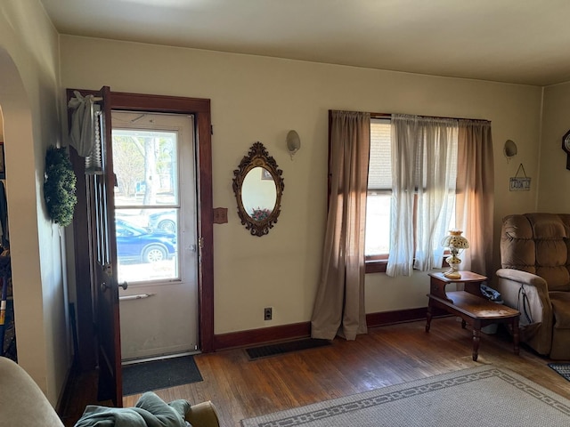 interior space with arched walkways, baseboards, visible vents, and hardwood / wood-style floors