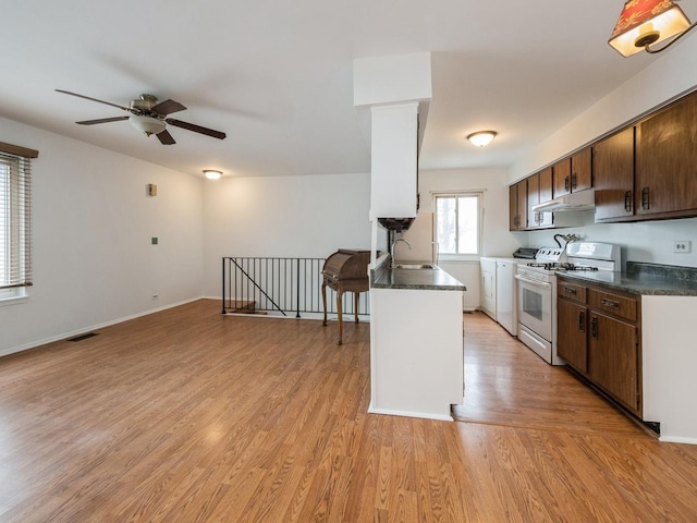 kitchen with white gas range, dark countertops, visible vents, a sink, and under cabinet range hood