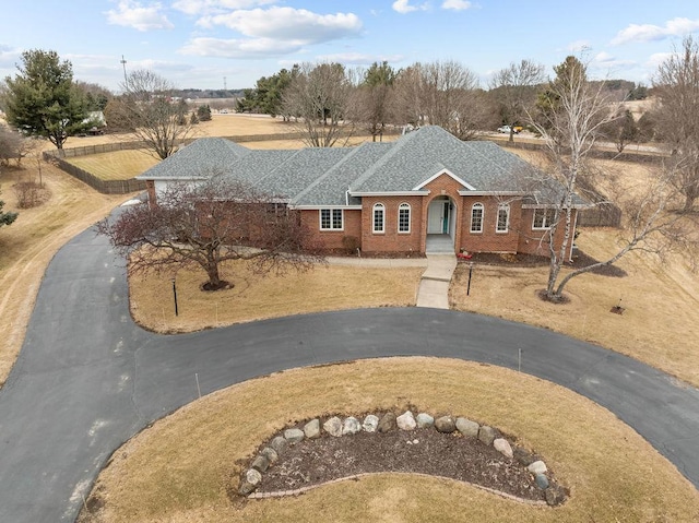 view of front of property with aphalt driveway, roof with shingles, fence, and brick siding