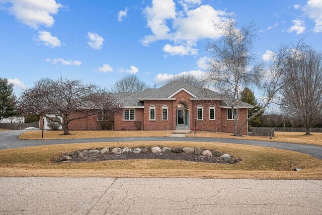 view of front facade with driveway, brick siding, roof with shingles, and fence