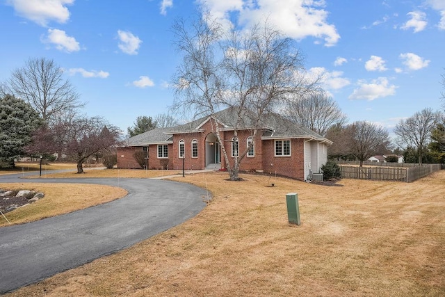 ranch-style home with aphalt driveway, a front lawn, fence, and brick siding