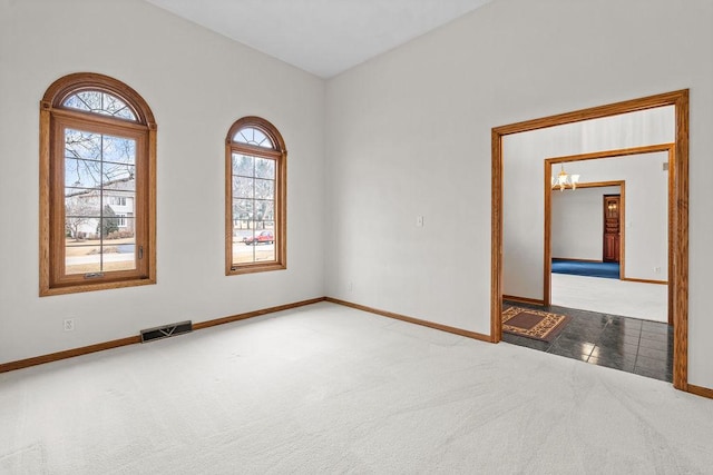 empty room featuring a chandelier, carpet, visible vents, and baseboards