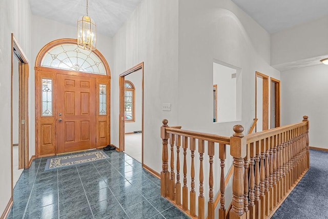 entrance foyer with a notable chandelier, a towering ceiling, baseboards, and dark tile patterned floors