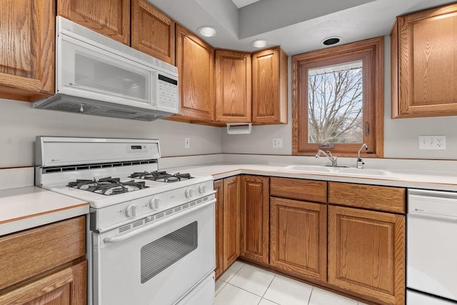 kitchen featuring light countertops, white appliances, a sink, and brown cabinets