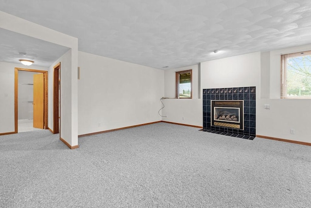 unfurnished living room featuring baseboards, a tiled fireplace, and carpet flooring