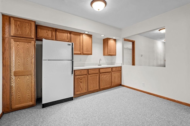 kitchen with baseboards, brown cabinets, freestanding refrigerator, light countertops, and recessed lighting