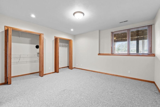 unfurnished bedroom with carpet, two closets, visible vents, and baseboards