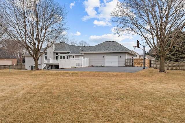 back of property with driveway, fence, a deck, and a lawn