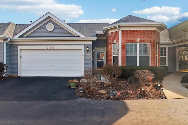 single story home with an attached garage, roof with shingles, aphalt driveway, and brick siding