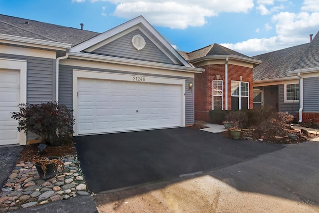 ranch-style home featuring aphalt driveway, an attached garage, brick siding, and a shingled roof