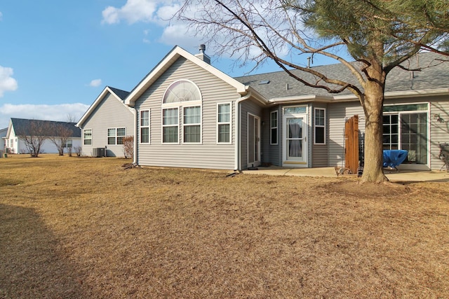 rear view of house featuring a shingled roof, central AC, a yard, and a chimney