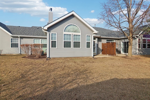 rear view of house with roof with shingles, a chimney, fence, and a yard