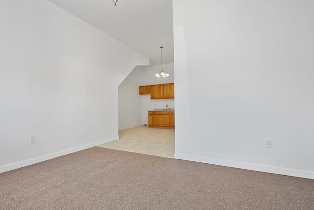 unfurnished living room featuring a notable chandelier, light carpet, a sink, baseboards, and vaulted ceiling