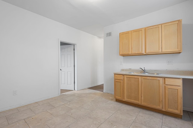 kitchen with light countertops, visible vents, light brown cabinets, a sink, and baseboards