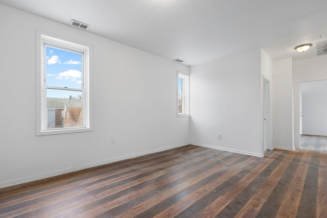 empty room with a healthy amount of sunlight, visible vents, and dark wood finished floors