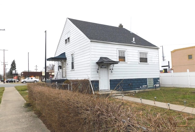 view of side of home with a chimney, fence, and roof with shingles