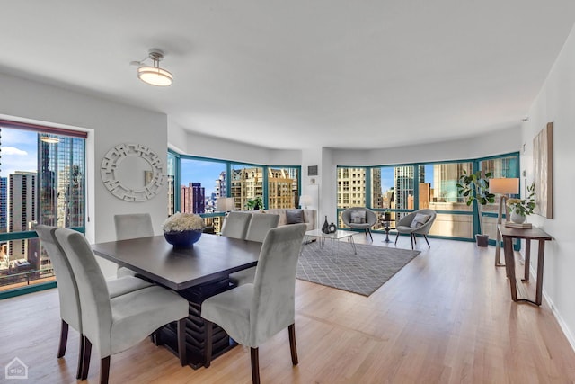 dining space featuring a view of city, light wood finished floors, plenty of natural light, and baseboards