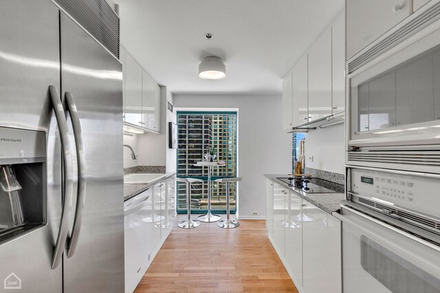 kitchen featuring light stone counters, light wood-style floors, white cabinets, a sink, and white appliances