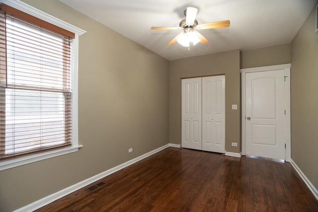 unfurnished bedroom featuring dark wood-style floors, baseboards, visible vents, and a closet