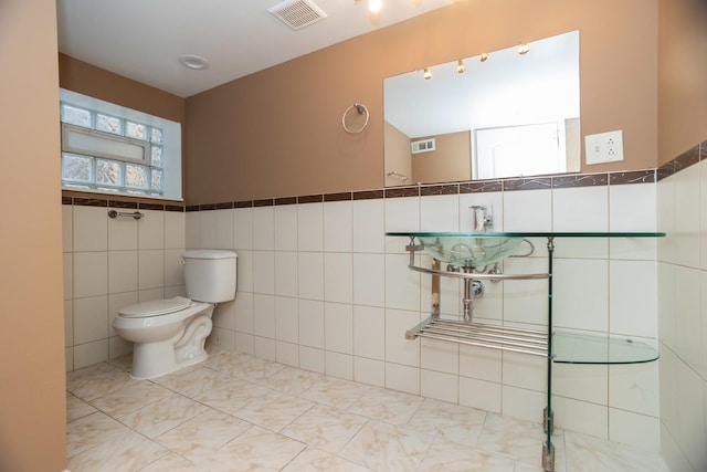 bathroom with toilet, visible vents, and tile walls