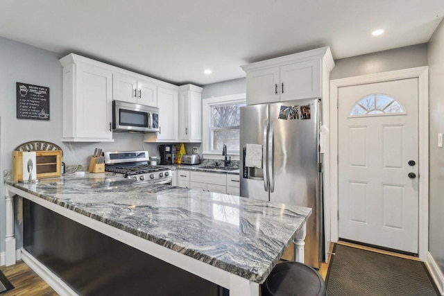 kitchen featuring dark stone countertops, stainless steel appliances, a peninsula, and a sink