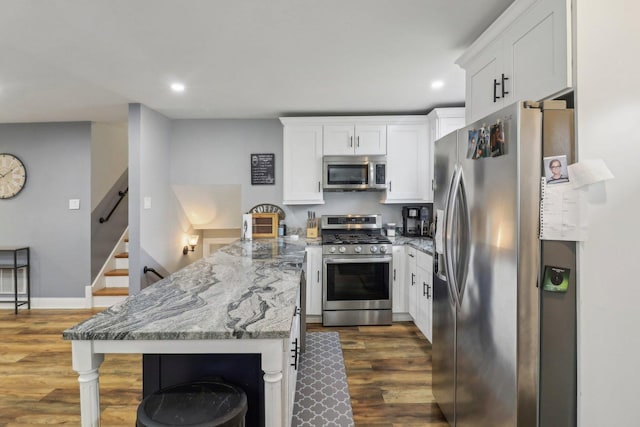 kitchen featuring stone counters, appliances with stainless steel finishes, white cabinets, a peninsula, and a kitchen bar