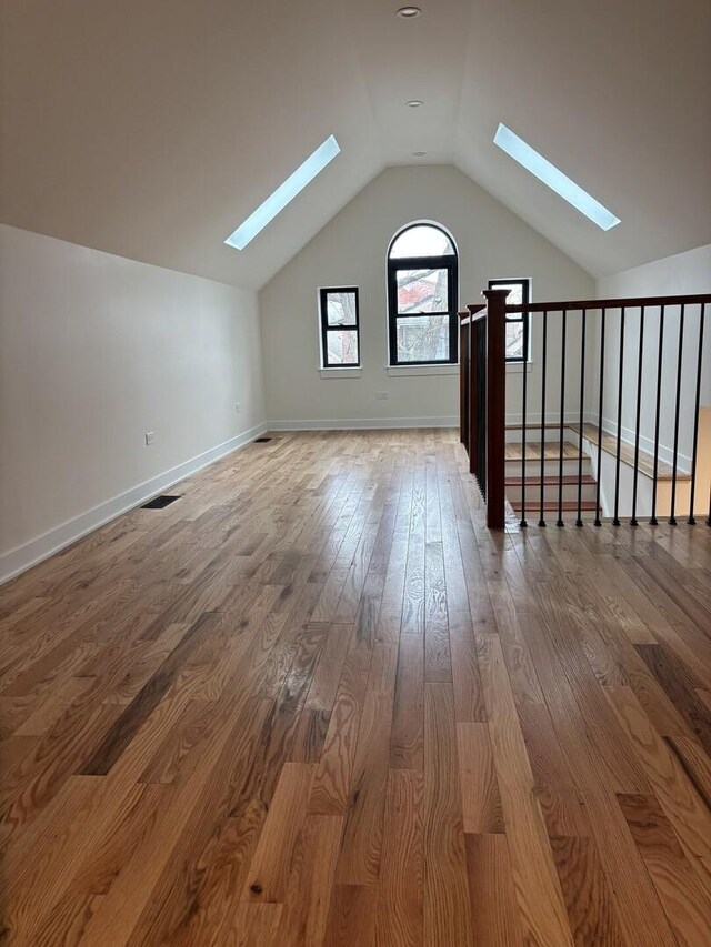 additional living space featuring baseboards, visible vents, wood finished floors, and lofted ceiling with skylight