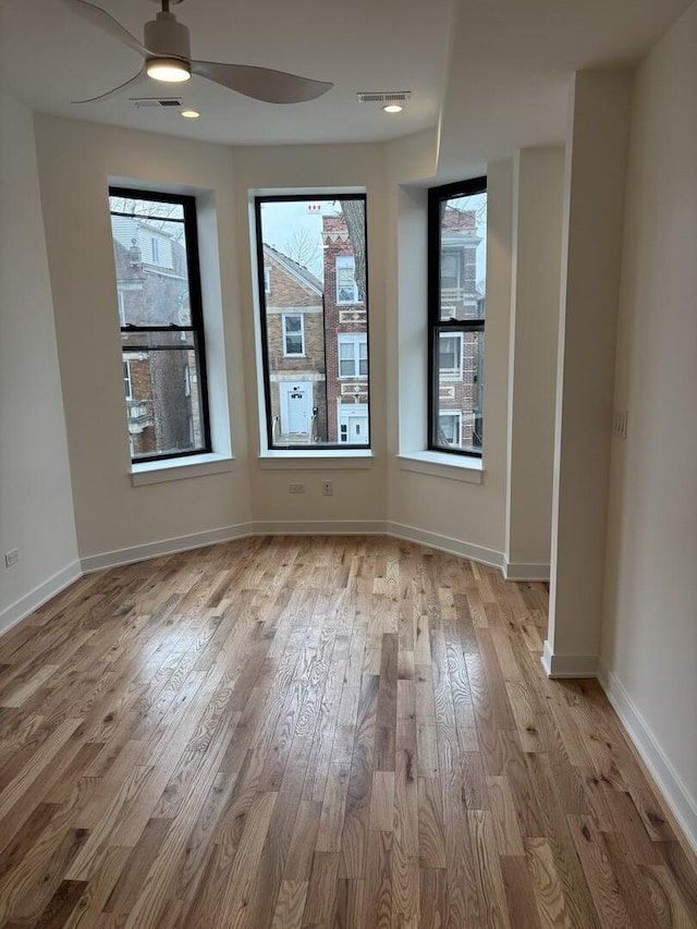 spare room featuring baseboards, visible vents, wood finished floors, and a ceiling fan