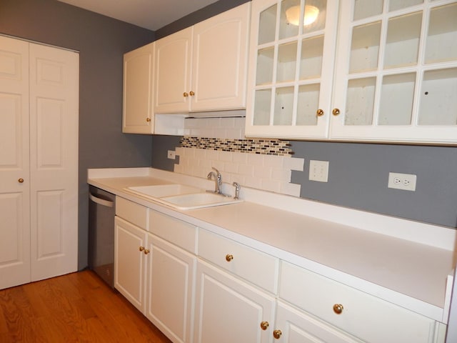 kitchen featuring dishwasher, light countertops, decorative backsplash, white cabinets, and a sink