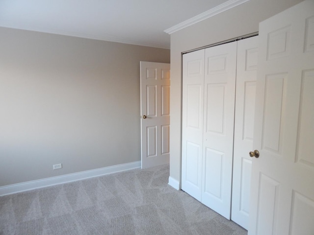 unfurnished bedroom with a closet, baseboards, light colored carpet, and crown molding