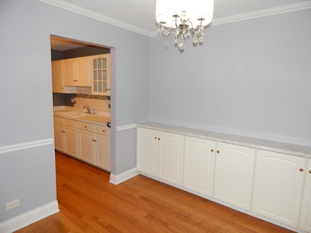 unfurnished dining area featuring baseboards, light wood-style flooring, a sink, crown molding, and a notable chandelier