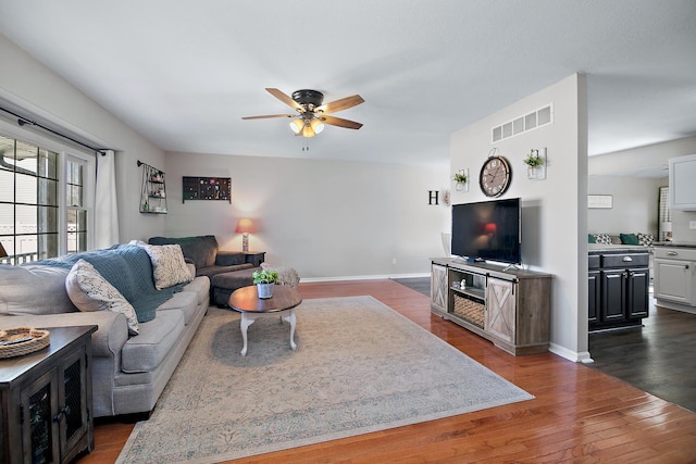 living room featuring dark wood-style floors, ceiling fan, visible vents, and baseboards