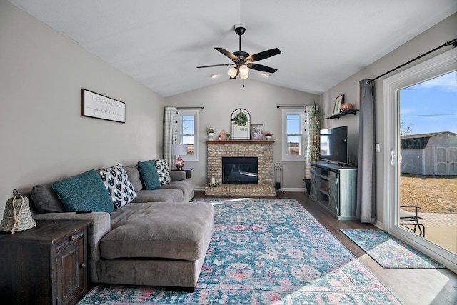 living area featuring baseboards, a ceiling fan, lofted ceiling, wood finished floors, and a fireplace