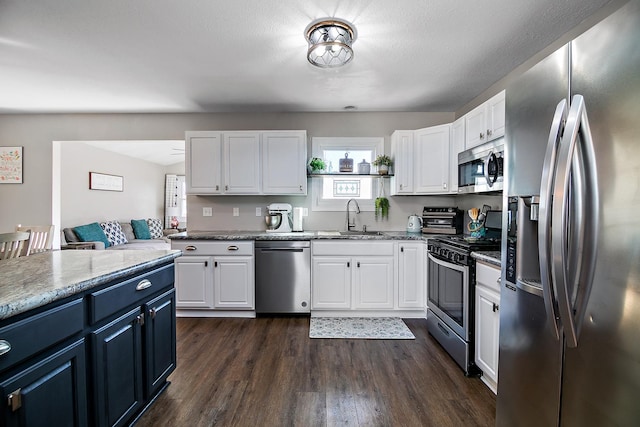 kitchen featuring white cabinets, appliances with stainless steel finishes, dark wood-style flooring, blue cabinets, and a sink