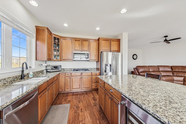 kitchen with dark wood finished floors, light stone counters, brown cabinets, stainless steel appliances, and a sink