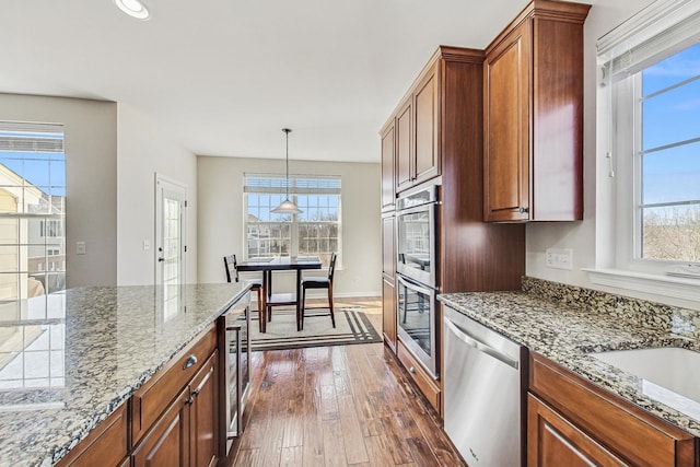 kitchen featuring dark wood-style floors, appliances with stainless steel finishes, light stone counters, and a wealth of natural light