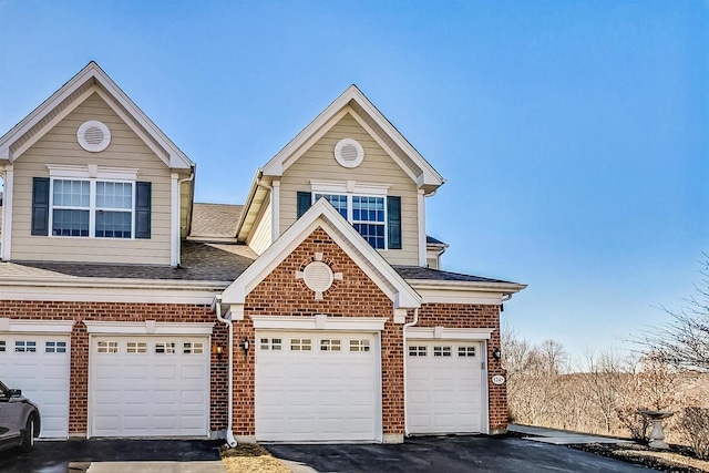 view of front of property featuring a garage, roof with shingles, aphalt driveway, and brick siding