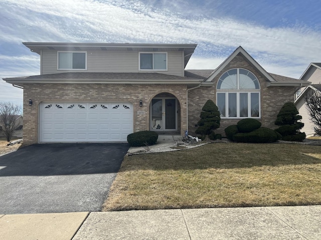 traditional home featuring a garage, aphalt driveway, a front yard, and brick siding