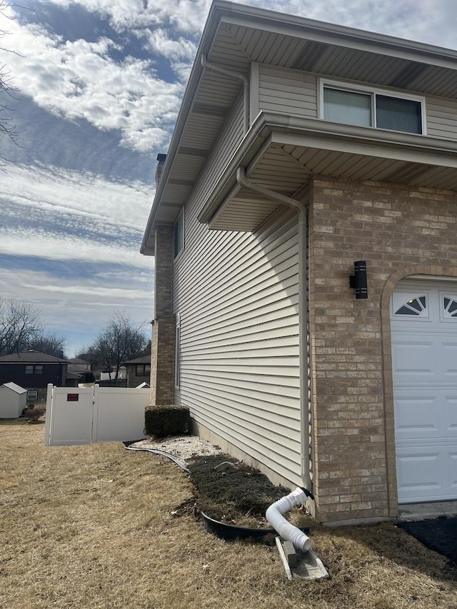 view of side of home featuring a garage, brick siding, and fence