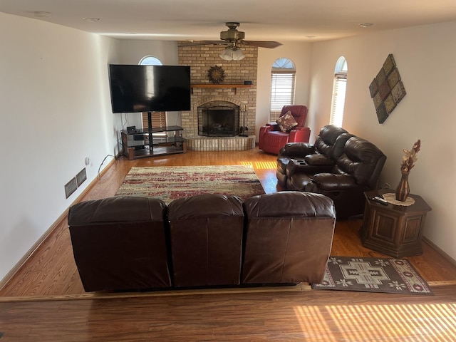 living area with visible vents, a brick fireplace, wood finished floors, and a ceiling fan