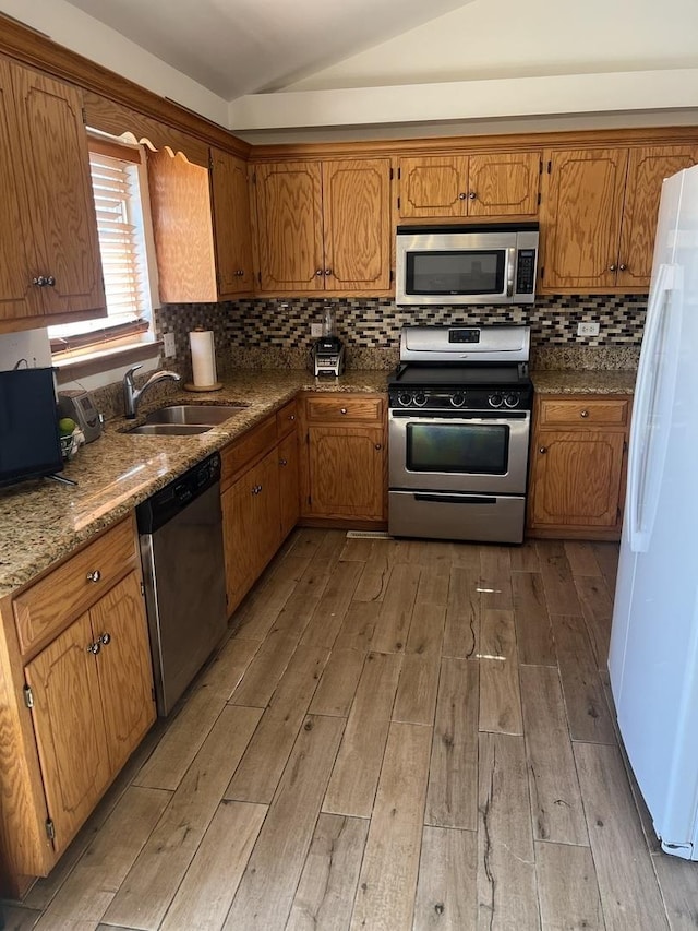 kitchen with tasteful backsplash, vaulted ceiling, stainless steel appliances, light wood-style floors, and a sink