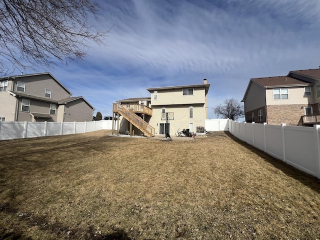 back of house featuring a fenced backyard, stairs, a lawn, a wooden deck, and a chimney