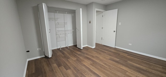 unfurnished bedroom featuring dark wood-style flooring, a closet, and baseboards