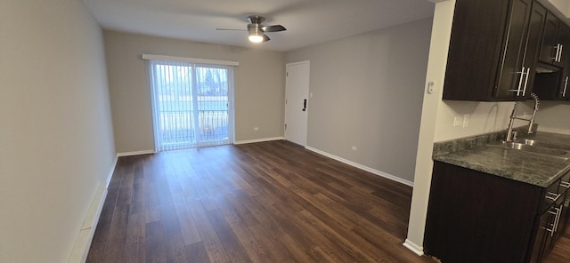 unfurnished dining area with a ceiling fan, a sink, dark wood finished floors, and baseboards