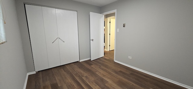 unfurnished bedroom with dark wood-type flooring, a closet, and baseboards